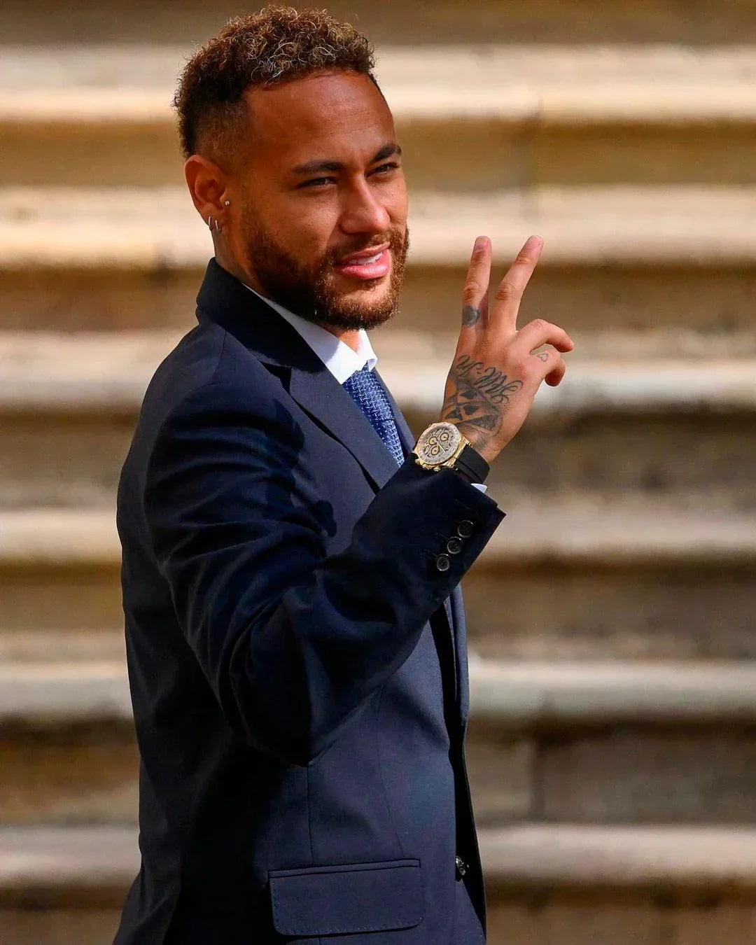 Man in suit wearing luxury men's watch, standing on stone steps and showing hand tattoo