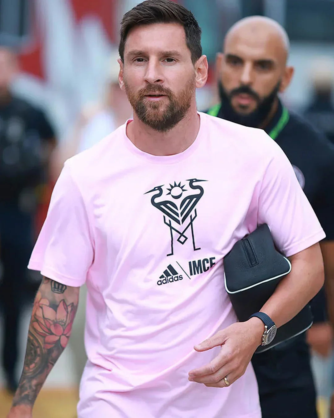 Man wearing a pink t-shirt, visible wristwatch, and carrying a pouch outdoors